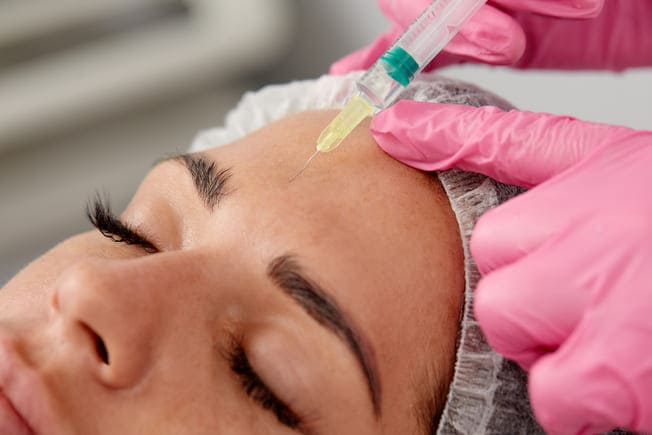 Inyección de bótox en la frente de una paciente en consulta